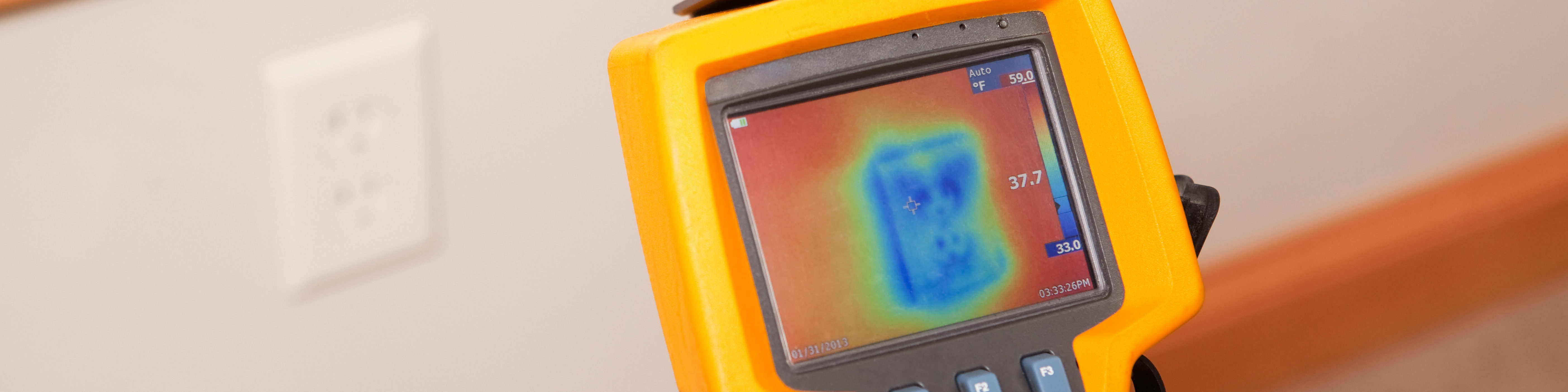 An infrared thermal imaging system being used during a home energy audit. The camera is pointed to a wall outlet, on an exterior wall, showing the blue (cold) area within the home’s insulation. The center target area reads 37.7 degrees with a range of 33 to 59 degrees in the area.  Energy audits are performed to determine how efficient the house is and to suggest steps to increase energy efficiency.